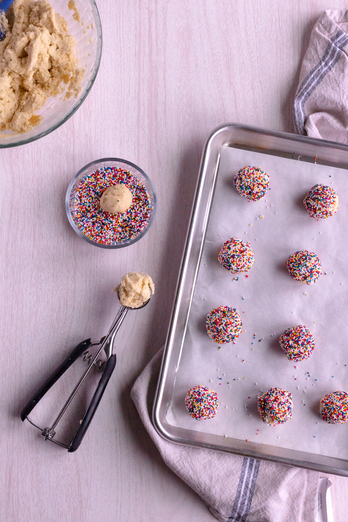 cookie dough balls being rolled in sugar and placed on a cookie sheet