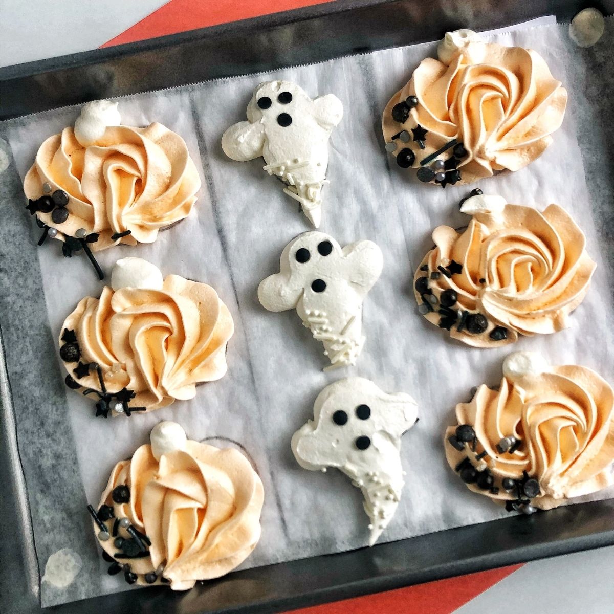 pumpkin and ghost meringue cookies on a baking sheet