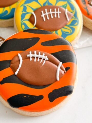 orange and black sugar cookie with a small football made of royal icing on it