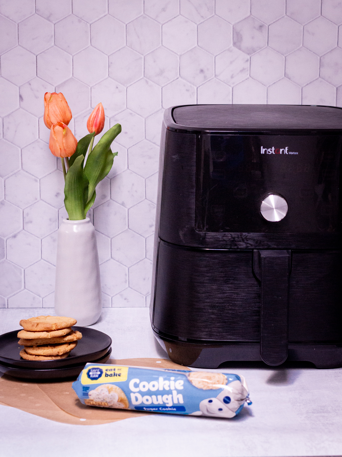 air fryer with roll of cookie dough and plate of baked cookies