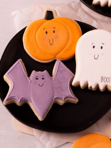 ghost, pumpkin, and bat cookies on a black plate