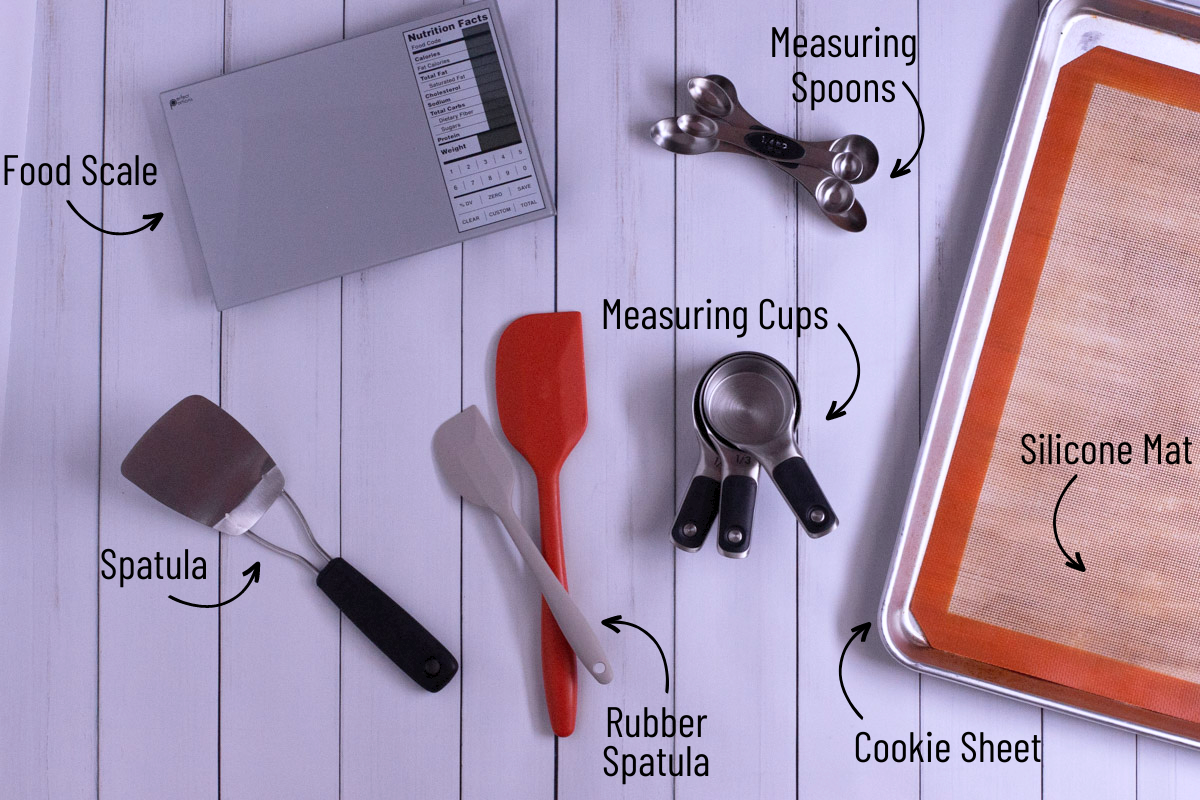 cookie baking supplies including silicone mat, cookie sheet, measuring cups, measuring spoons, spatulas, and a food scale