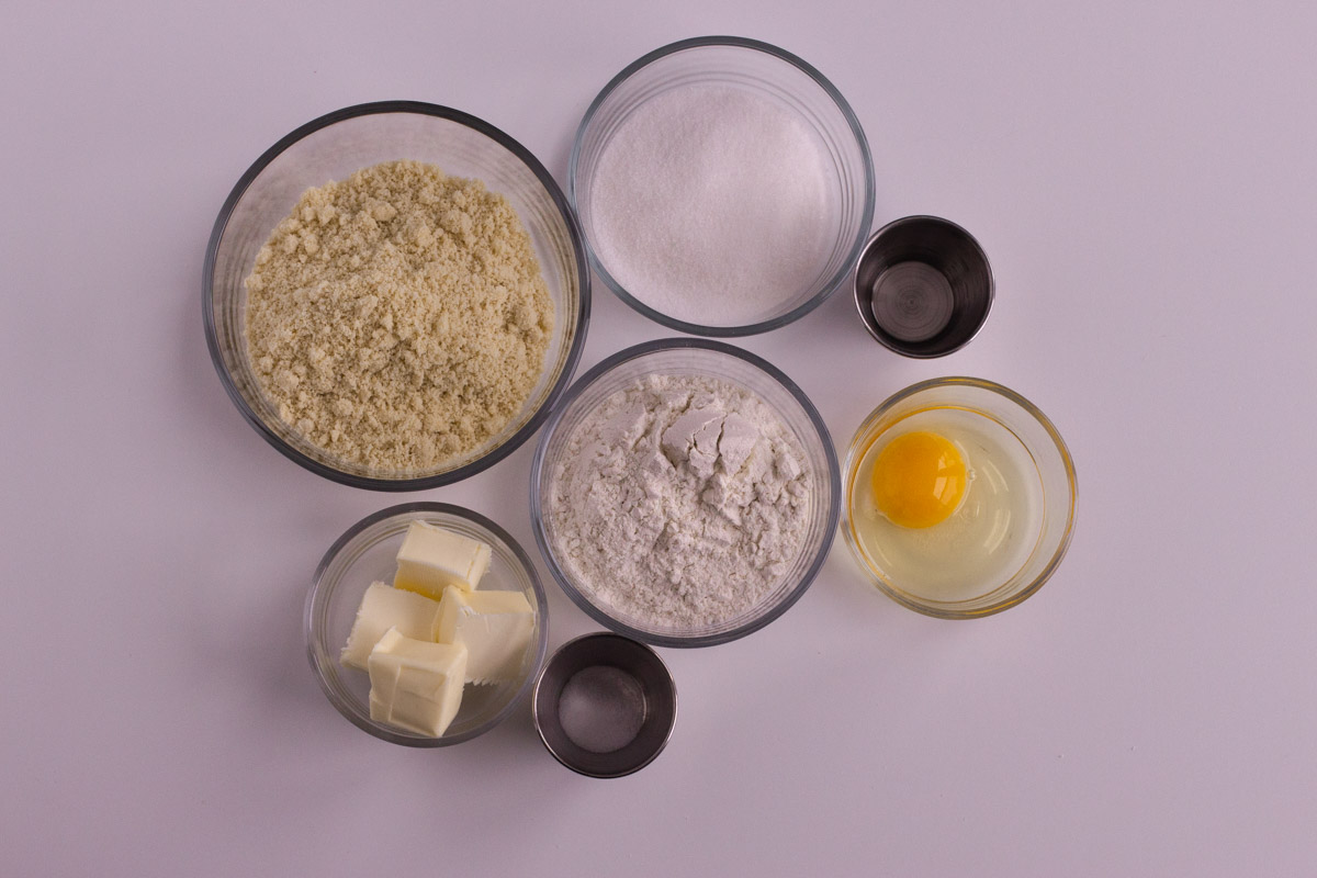 All of the ingredients for almond sugar cookies laid out in individual bowls.