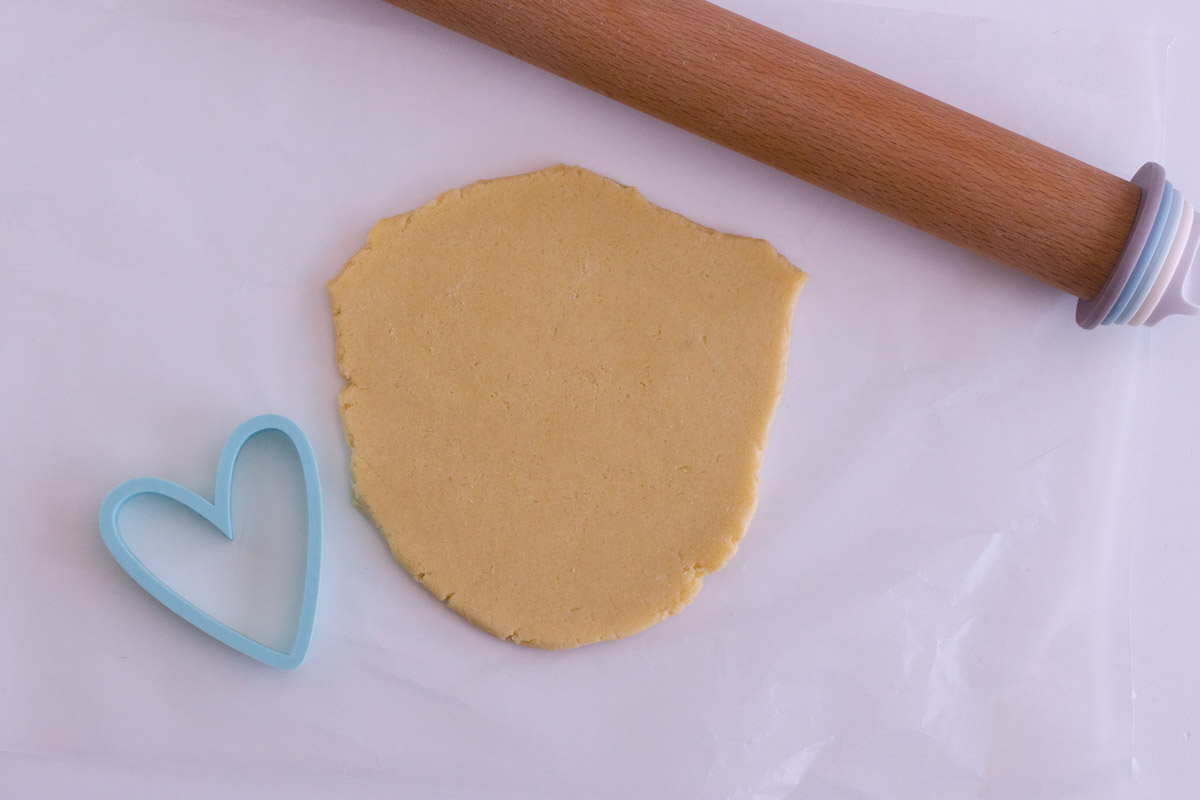 Cookie dough rolled out next to cookie cutter and rolling pin.