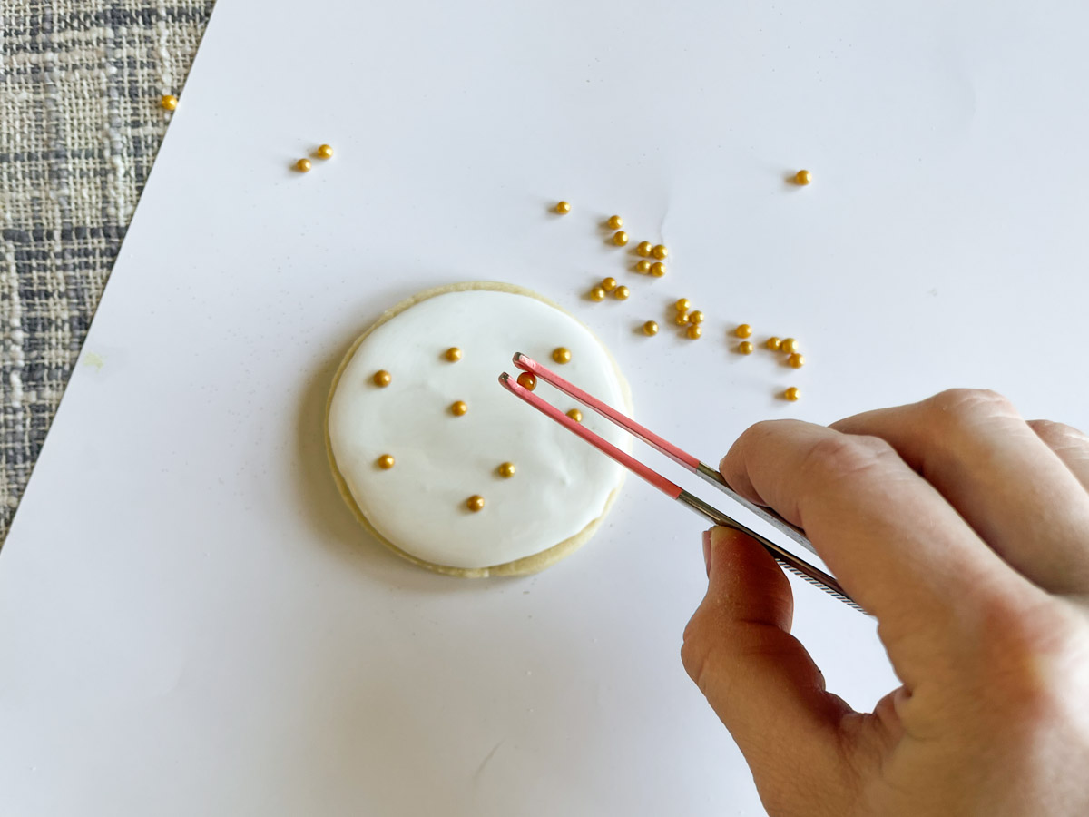 adding sugar pearls to royal icing cookie