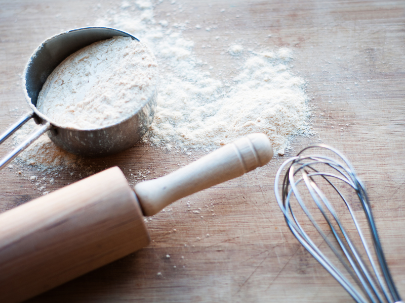 measuring cup, whisk, and rolling pin with flour on a butcher block