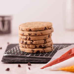 Stack of 6 chocolate chip cookie cutouts next to 3 bags of royal icing