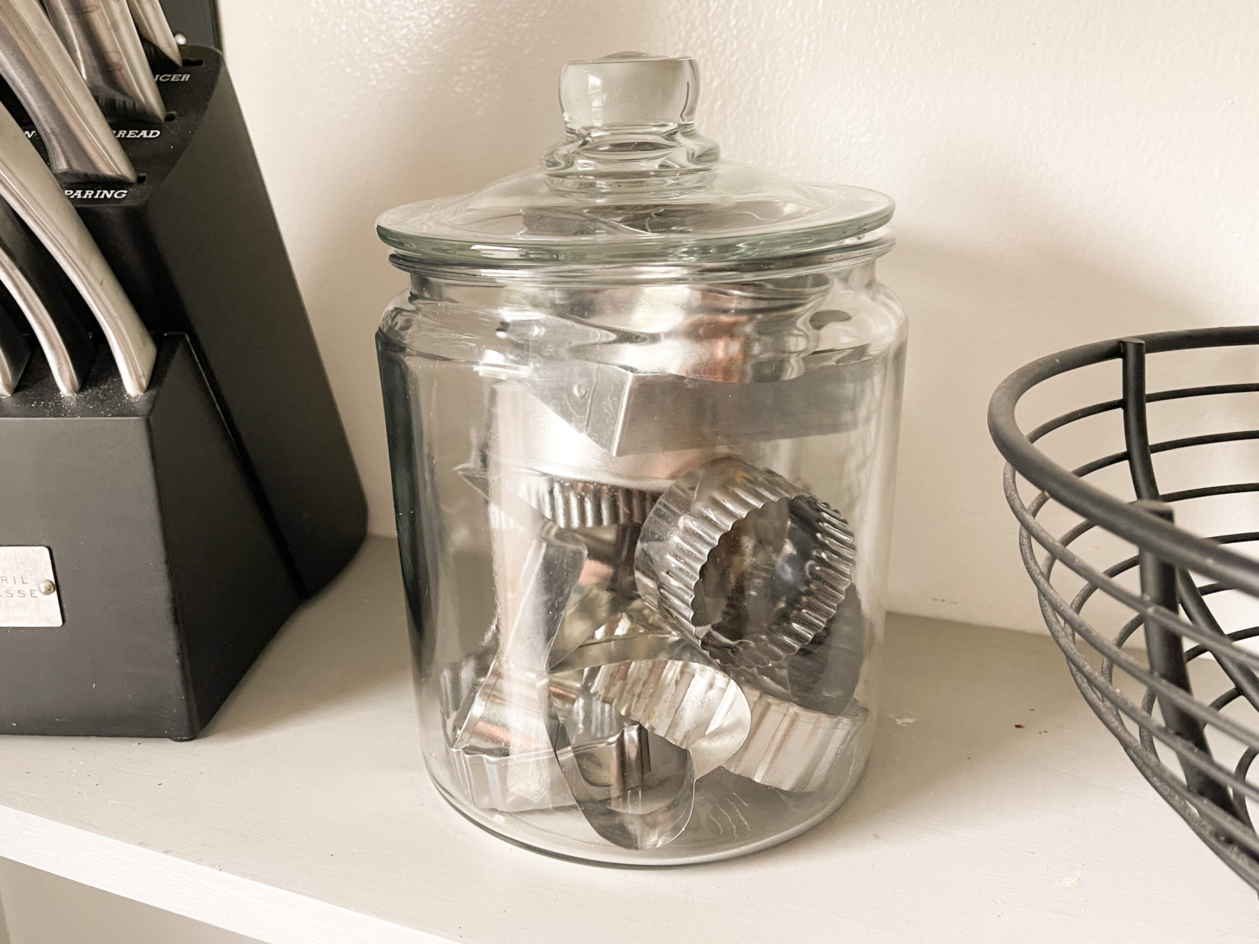 Clear glass cookie jar filled with metal cookie cutters