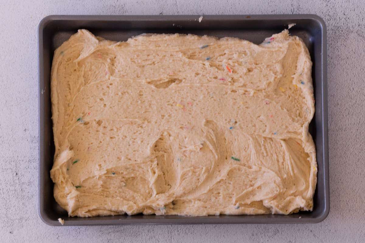 Cookie dough spread out evenly across a 9x13 brownie pan. 