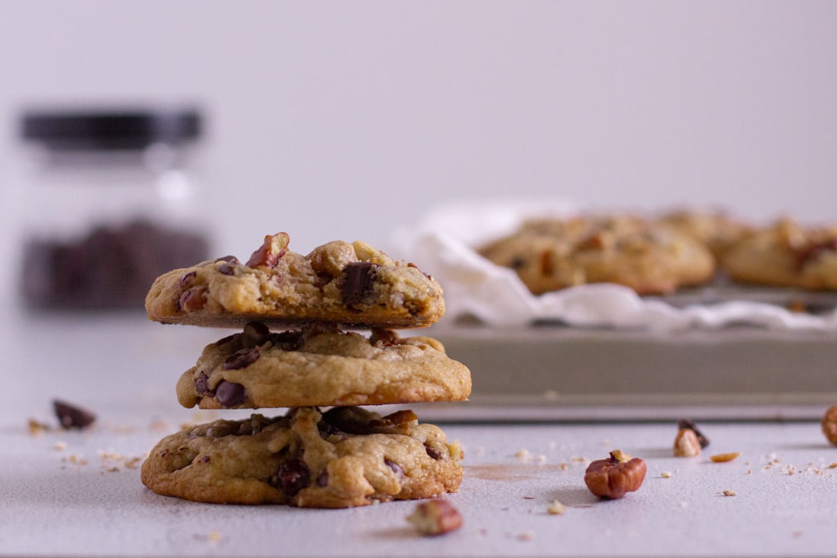 3 pecan chocolate chip cookies stacked up with crumbs and pecans around