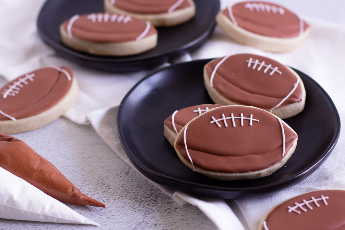 Football cookies on a plate with brown and white royal icing bags.