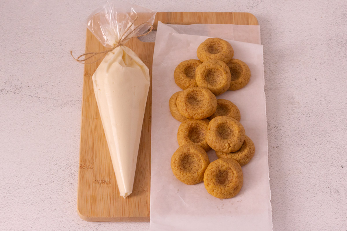 Baked thumbprint cookies with cream cheese frosting in piping bag.