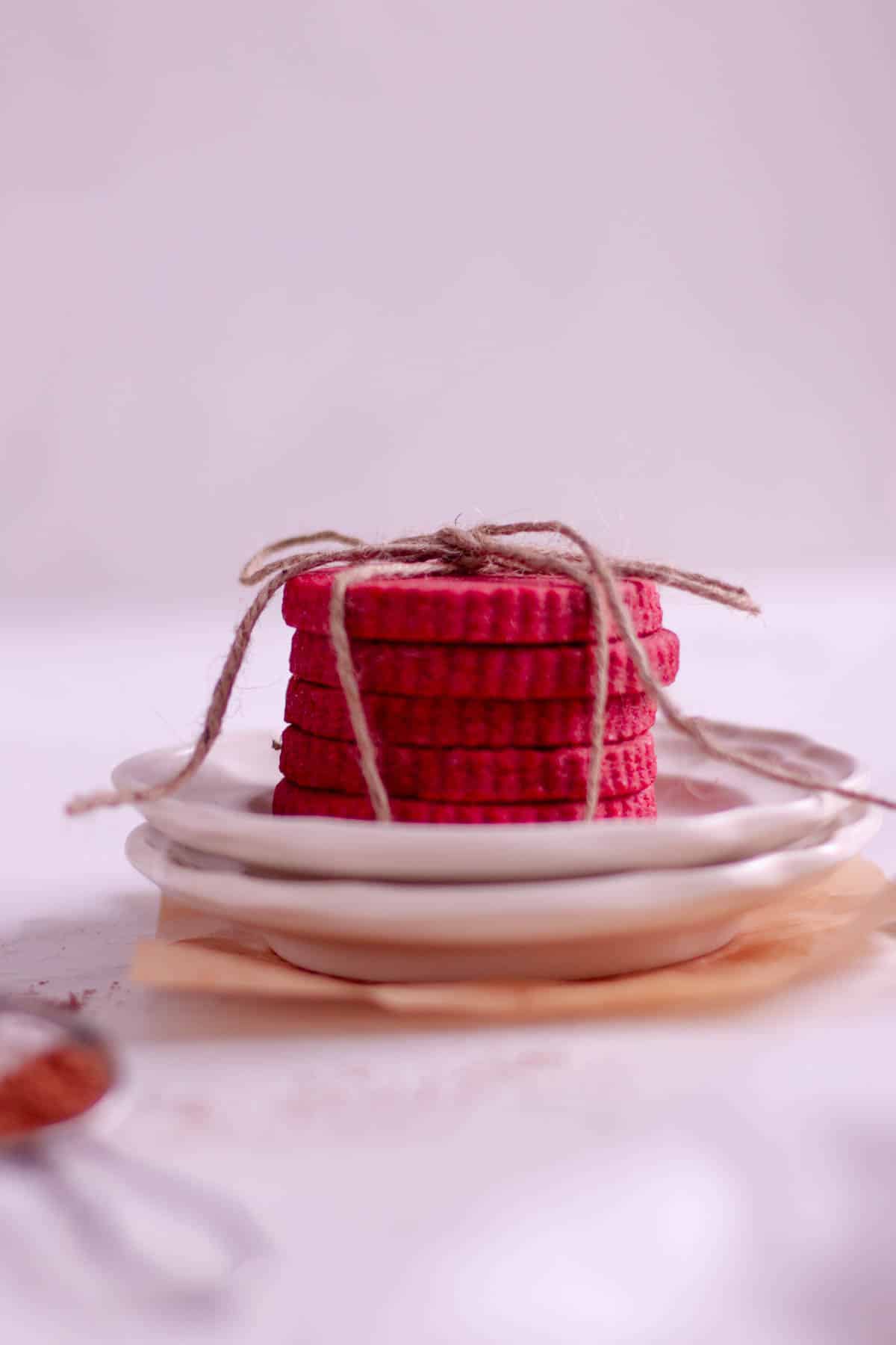 Stack of red velvet cut out cookies on a plate and tied together with a piece of twine. 