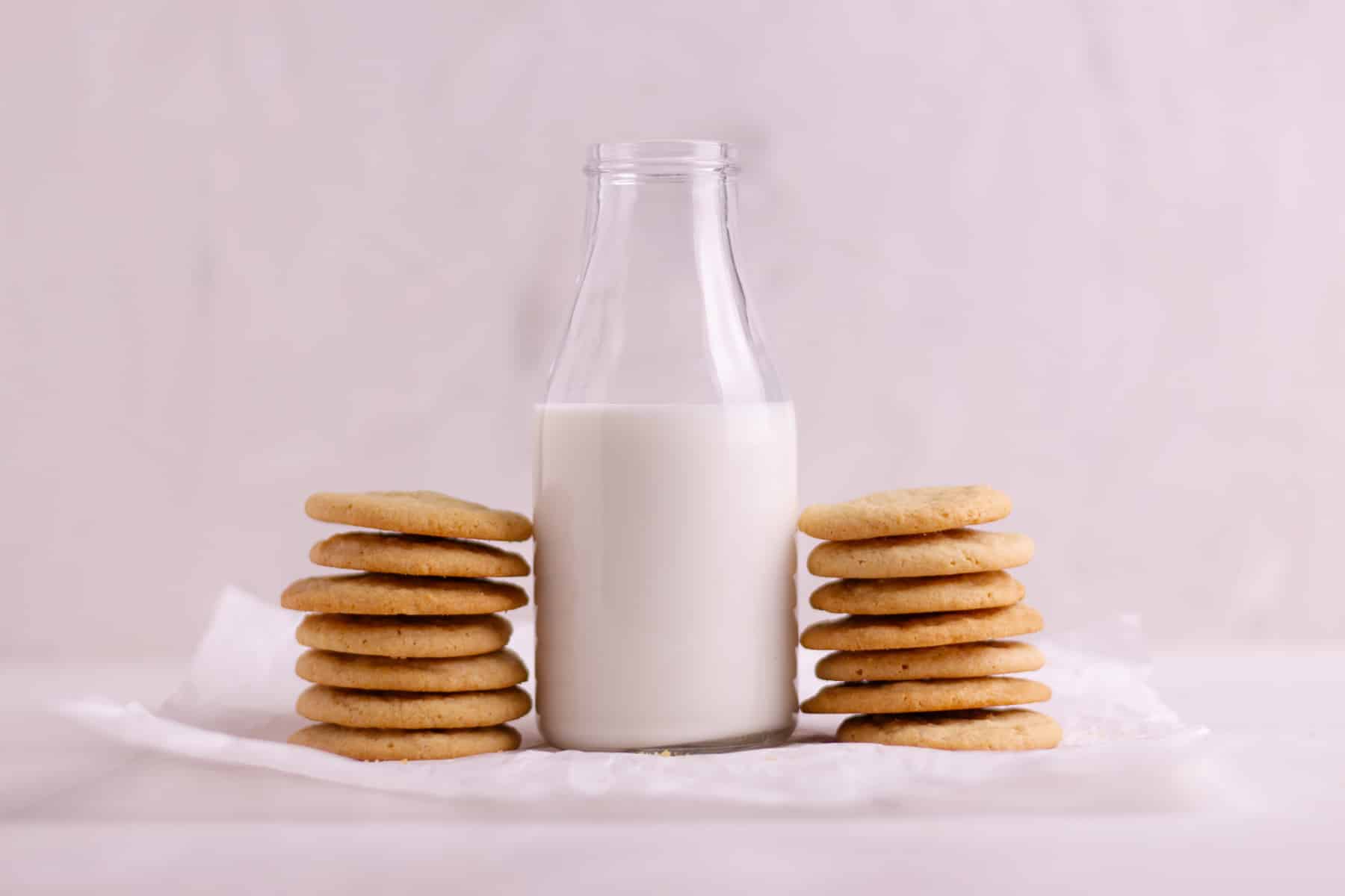 Small bottle of milk with two stacks of cookies.